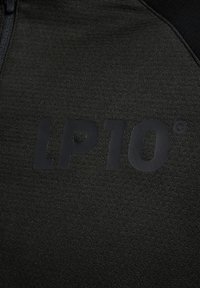 Zwarte stof met een textuur oppervlak, voorzien van een prominent matzwart "LP10" logo. Het materiaal is zacht en het ontwerp is strak en modern.