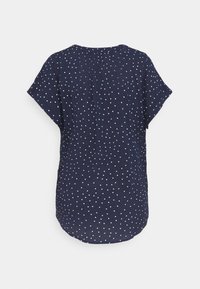 Blouse marine à pois avec des manches courtes, un col rond et un détail de pli à l'arrière ; le tissu est lisse avec une texture légère.