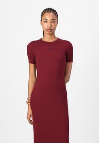 Burgundy ribbed dress with short sleeves, round neckline, and subtle logo detail. Smooth texture and fitted silhouette.