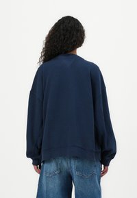 Felpa oversize blu navy con collo a giro e spalle scese, con polsini e orlo a coste, mostrata da dietro.