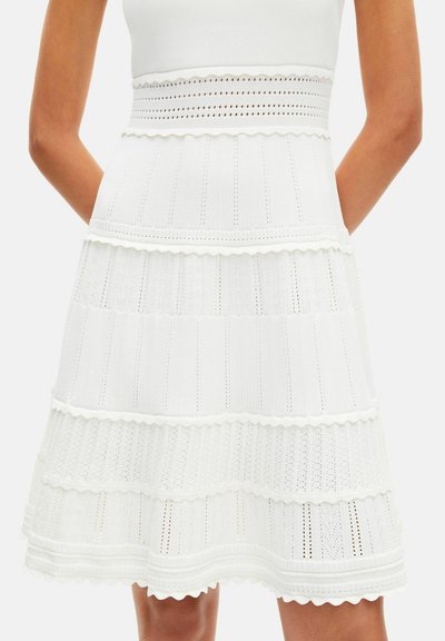 Falda blanca de punto en línea A con rayas horizontales texturizadas y bordes ondulados, combinada con una camiseta blanca sin mangas.