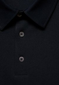 Čierna polo tričko s textúrovanou tkaninou, preloženým golierom a tromi čiernymi gombíkmi na légii. Detailný pohľad zdôrazňuje materiál a dizajn.