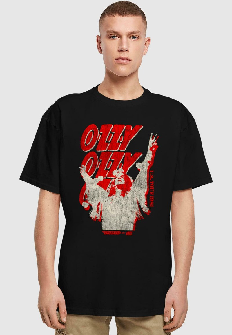 Juodas medvilnės marškinėliai su nusidėvėjusiu raudonu ir baltu piešiniu, vaizduojančiu figūrą su pakeltom rankom ir užrašu: "OLLY OLLY U.S. TOUR 1981."