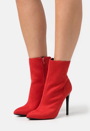 Red suede ankle boots with a pointed toe, side zipper, and a high stiletto heel. Smooth texture and fitted silhouette.