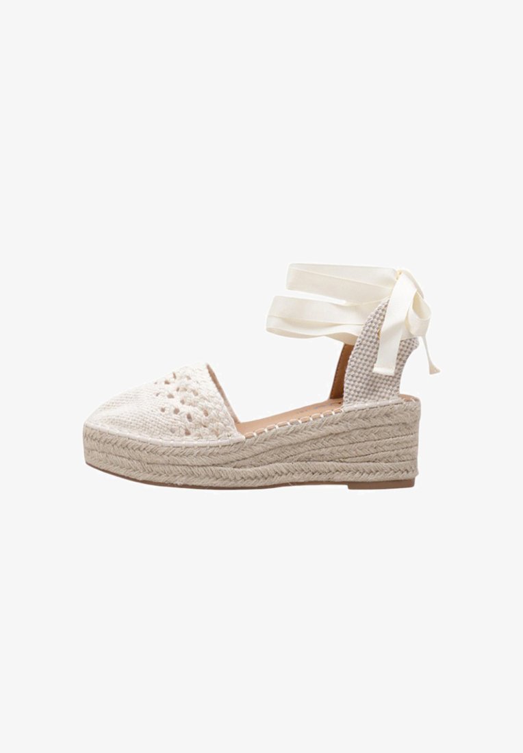 Sandal de cuña blanca estilo espadrille con parte superior de tela tejida, punta abierta y lazos en el tobillo de cinta. La suela trenzada de yute añade textura y altura.