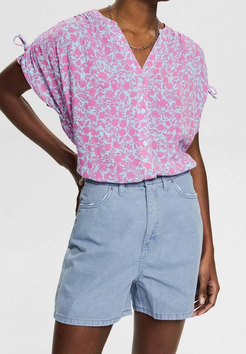 Roze en blauwe bloemenprint blouse met korte mouwen en knoopsluiting, gecombineerd met lichtblauwe denim shorts. De blouse heeft geplooide mouwen.