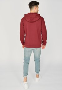 Bordowa bluza z kapturem, wykonana z miękkiego materiału, w połączeniu z jasnoniebieskimi dżinsami slim-fit i białymi trampkami, widok z tyłu.