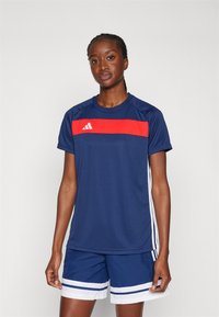 Marineblauw sportshirt met een rode horizontale streep, korte mouwen en drie witte strepen aan de zijkanten, gecombineerd met marineblauwe shorts en witte accenten.