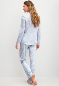 Ensemble de pyjama bleu clair avec un motif d'étoiles. Le haut à manches longues et le pantalon présentent une texture douce et une coupe décontractée, adaptés pour le sommeil.