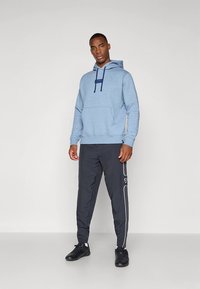 Sweatshirt azul-claro com capuz, cordões azul-marinho e bolso canguru central, combinado com calças desportivas cinzento-escuro com riscas brancas nas laterais.