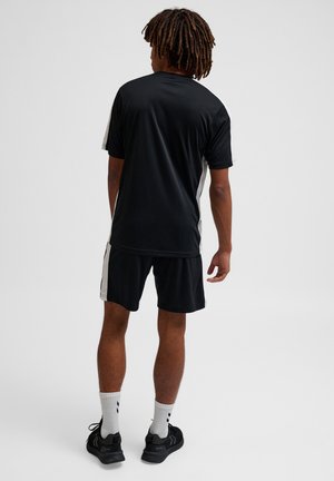 Zwart sportshirt en shorts met witte zijstrepen, korte mouwen en een ronde halslijn. Draag het met witte sokken en zwarte sneakers.