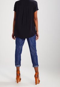 Sort kortærmet top med buet kant, parret med blå jeans med optrukne ærmer og orange højhælede sandaler med et struktureret design.