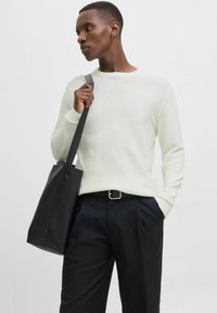 Pull à côtes de couleur claire avec des manches longues, associé à un pantalon plissé sombre et un sac tote noir texturé. Design simple, look moderne.
