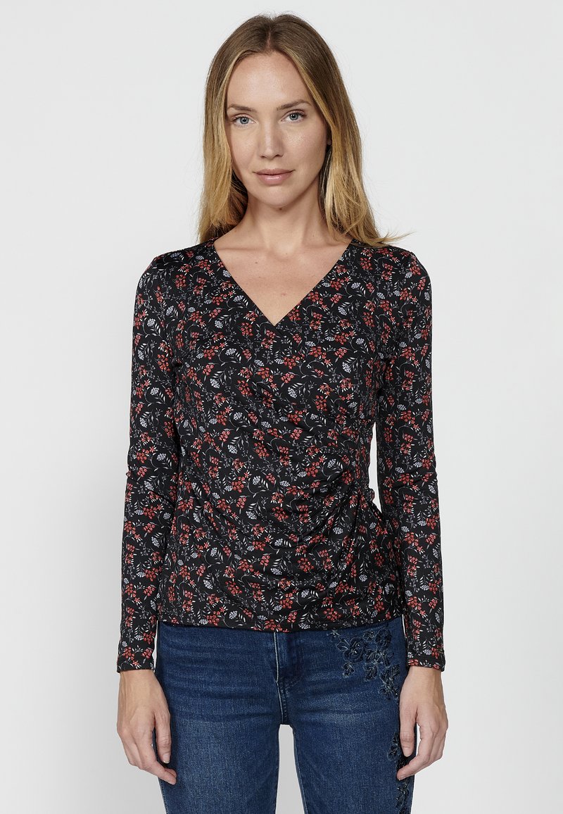 Schwarzes Langarmoberteil mit V-Ausschnitt, das ein florales Muster in Rot und Weiß aufweist. Der Stoff hat eine weiche Textur und ein Raffungdesign an der Taille.