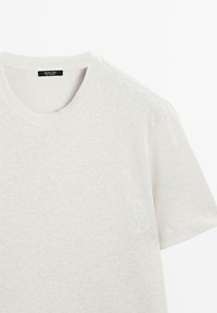 Světle šedé bavlněné tričko s kulatým výstřihem a krátkými rukávy. Jemná textura s mírným melírovaným vzorem. Nálepka viditelná uvnitř výstřihu.