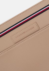 Article en cuir beige texturé avec un logo Tommy Hilfiger cousu et un détail en tissu rayé rouge, blanc et noir.