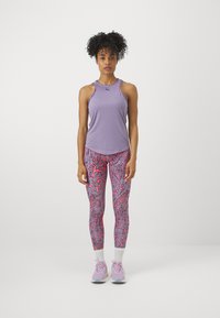 Lila sportos ujjatlan felső, vállvágásokkal, pink absztrakt mintás leggingszel párosítva. A világoslila sportcipők teszik teljessé a megjelenést.