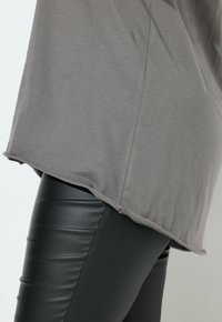 Szary bawełniany top z okrągłym hemem, w połączeniu z czarnymi legginsami z sztucznej skóry, eksponujący gładką fakturę i elegancki design.