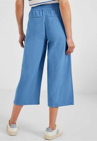 Blauwe linnen wijde broek met een elastische tailleband en twee achterzakken, gecombineerd met witte sneakers met grijze accenten.
