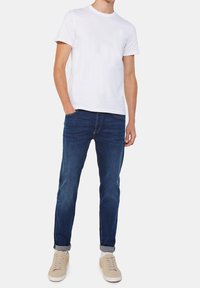 White short-sleeve t-shirt, dark blue slim-fit jeans, and beige sneakers. Jeans feature rolled cuffs; t-shirt has a classic crew neck design.