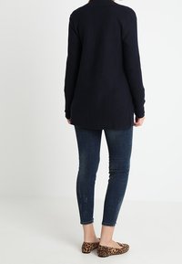 Granatowy prążkowany kardigan z długimi rękawami, bez zapięcia z przodu i dłuższym tyłem. Noszony z ciemnymi dopasowanymi jeansami i balerinami w cętki lamparta.