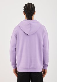 Felpa di cotone viola con cappuccio, maniche lunghe e vestibilità comoda. I dettagli delle cuciture e i polsini a coste conferiscono struttura.