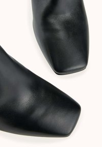 Chaussures en cuir noir avec une texture lisse et un design à bout carré. Les chaussures ont une finition polie et une silhouette épurée.
