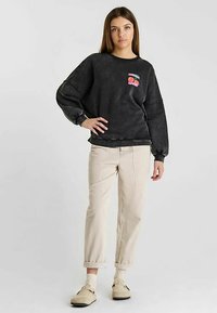 Sweat-shirt noir avec motif graphique, coupe décontractée et manches bouffantes. Associé à un pantalon en velours côtelé beige et des chaussures de couleur claire.