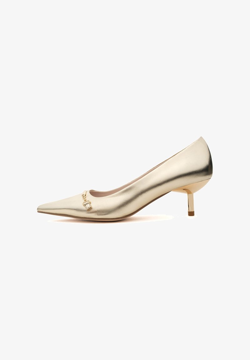 Pumps metallici dorati con punta affusolata, dotati di un piccolo ciondolo decorativo sul collo del piede e di un tacco basso con dettagli dorati. Texture liscia.