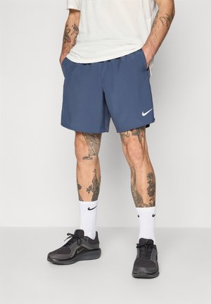 Granatowe szorty sportowe z elastycznym paskiem, bocznymi kieszeniami i białym logo Nike. Noszone z białymi skarpetkami i czarnymi butami sportowymi.