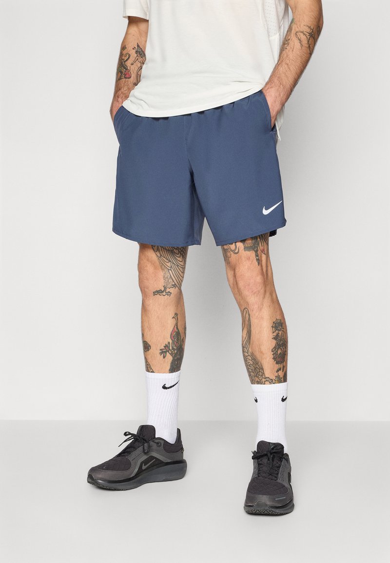 Navy blue athletic shorts with an elastic waistband, side pockets, and a white Nike logo. Worn with white socks and black athletic shoes.