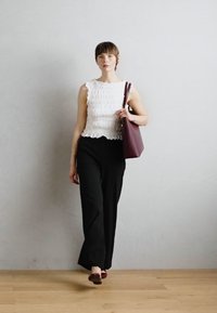 Haut sans manches blanc et texturé, pantalon large noir et sac en bandoulière bordeaux. Chaussures plates marron. Fond neutre avec un sol en bois. Design simple.