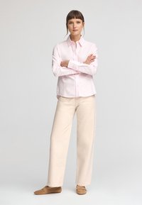 Ljust rosa skjorta med knappar och långa ärmar; avslappnad passform; matchad med ljusbeiga vida byxor och bruna slip-in skor. Rena linjer och mjukt tyg.