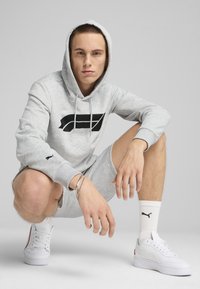 Hanorac gri cu logo negru, pantaloni scurți gri asortați, adidași albi și șosete albe cu logo. Design minimalist, material din amestec de bumbac.