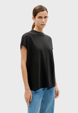 Haut noir à manches courtes en coton, avec un col rond et une coupe ample, associé à un jean bleu clair pour le contraste.