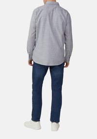 Grijze ruitjes overhemd met lange mouwen en een button-down kraag, gecombineerd met blauwe spijkerbroek en witte sneakers, bekeken vanuit de achterkant.