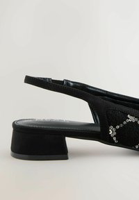 Sort slingback sko med en lav, firkantet hæl, der har en struktureret overdel og dekorative pailletter arrangeret i et geometrisk mønster.