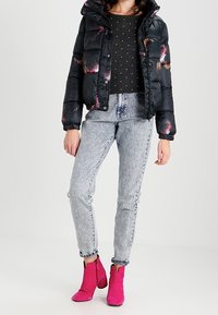 Czarna puchowa kurtka z kolorowymi wzorami piór, szary sweter w kropki, jasne dżinsy i różowe botki za kostkę.