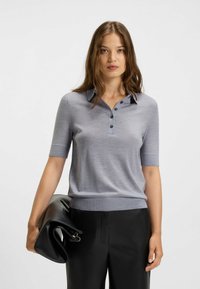 Polo shirt grigio a maniche corte in materiale morbido, con colletto e placca di tre bottoni, abbinato a pantaloni di pelle neri e una pochette.