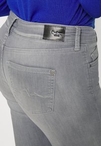 Vaqueros grises con una textura suave, que cuentan con una etiqueta de cuero negro y un bolsillo trasero con un patrón de costura decorativa.