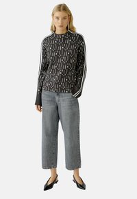 Zwart gebreid trui met een wit abstract patroon, gecombineerd met grijze jeans met hoge taille en wijde pijpen, en zwarte puntige flats.