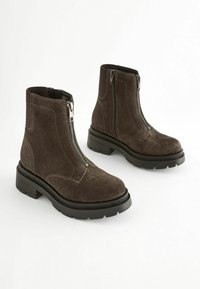 Bruine suède enkelboots met een zijrits, textuur op de schacht en een stevige zwarte rubberen zool. Voorzien van elastische zijpanelen voor extra flexibiliteit.