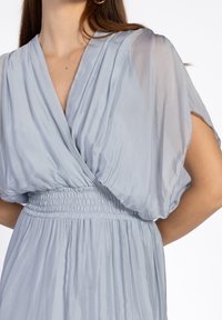 Lichtblauwe jurk van een gestructureerde, vloeiende stof. Beschikt over een V-halslijn, opgeblazen mouwen en een elastische taille voor een relaxte pasvorm.