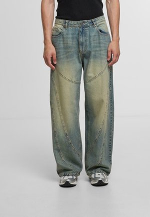 Helle blaue Denim-Jeans mit weitem Bein, ausgestattet mit einem verblassten Farbverlauf, geschwungenen Nähten und klassischem Fünf-Taschen-Design. Dazu werden graue Sneakers getragen.