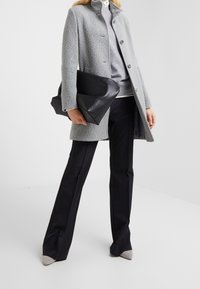 Grå, texturerad kappa med hög krage och knappstängning, kombinerad med en grå tröja, svarta byxor och en stor svart kuvertväska.