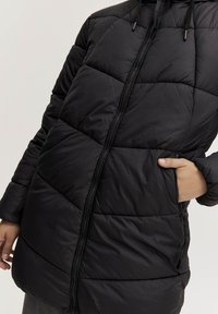 Svart pufferjacka med dragkedja, med horisontella quiltade paneler, hög krage och sidofickor. Slät tygtextur.