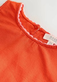 Rotes Leinenoberteil mit einem runden Halsausschnitt und einem pinkfarbenen gewellten Saum sowie einemverschluss auf der Rückseite. Es zeichnet sich durch eine glatte Textur und ein lässiges Design aus.