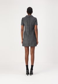 Kortärmad, grå rutmönstrad klänning med krage, dragkedja bak och figursydd silhuett, tillsammans med svarta klackar och strumpor.