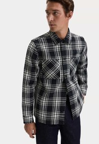 Czarna i biała koszula w kratkę z zapięciem na guziki, kołnierzykiem, długimi rękawami oraz strukturalną tkaniną w deseń kratki.