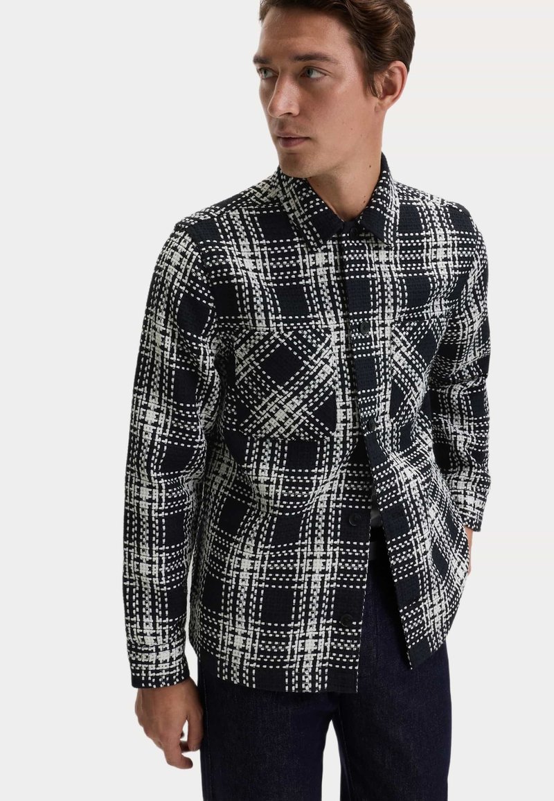 Czarna i biała koszula w kratkę z zapięciem na guziki, kołnierzykiem, długimi rękawami oraz strukturalną tkaniną w deseń kratki.